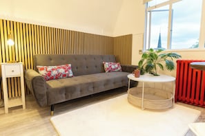A modern living room with a grey sofa, a small white side table, a round white side table, a potted plant, and a red radiator.