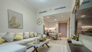 A modern living room with a white sofa, a coffee table, and a dining area with a chandelier. - Chic Meydan Apt with Balcony and City & Pool Views-1012 (Dubai)