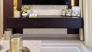 A modern living room with a large flat-screen TV mounted on a dark wooden console, a glass vase with flowers, and framed pictures on the console. - Chic Meydan Apt with Balcony and City & Pool Views-1012 (Dubai)