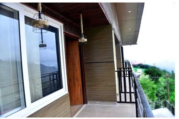 A balcony with a wooden floor, a glass door, and two hanging light fixtures. - The Dhanaulti chalet (Dhanaulti)