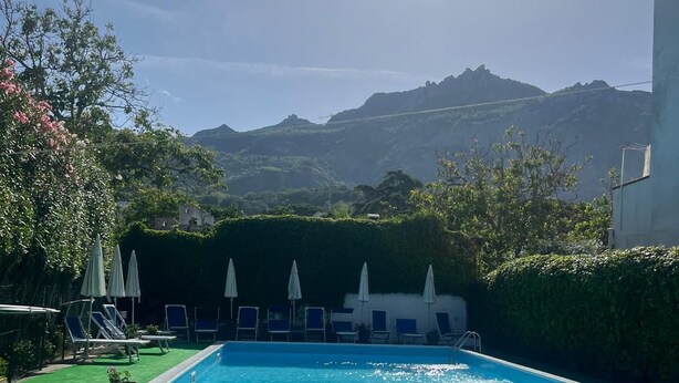 A swimming pool with a view of mountains in the background, surrounded by lounge chairs and umbrellas. - Perla Bianca Holiday Home Ischia, Forio, nei pressi dei giardini Poseidon (Forio, Ischia (Na))