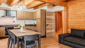 Une cuisine moderne avec des meubles en bois, une table à manger avec des chaises et un canapé noir dans l’espace salon.