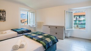 A bedroom with a bed, two pillows, a bedside table, a radiator, and a window with a view of buildings. - GuestHost - Charming 100 sqm detached villa, spread over three levels (accessible by stairs) and accommodating up to 5 people.The property is located in Lierna, on the eastern shore of Lake Como, in a well-served area and a short walk from the splendid R (Lierna)