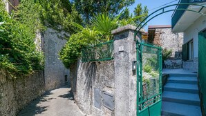 A narrow stone pathway leading to a gated entrance with a stone pillar marked with the number 5. - GuestHost - Charming 100 sqm detached villa, spread over three levels (accessible by stairs) and accommodating up to 5 people.The property is located in Lierna, on the eastern shore of Lake Como, in a well-served area and a short walk from the splendid R (Lierna)