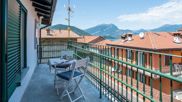 A balcony with a table and chairs, a green railing, and a view of terracotta-roofed buildings and mountains. - GuestHost - Charming 100 sqm detached villa, spread over three levels (accessible by stairs) and accommodating up to 5 people.The property is located in Lierna, on the eastern shore of Lake Como, in a well-served area and a short walk from the splendid R (Lierna)