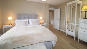 A bedroom with a large bed, two bedside tables with lamps, a wardrobe, and a door leading to another room. - Clarmes House (Limavady)