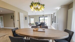A spacious dining area with a round wooden table surrounded by six chairs, a hanging light fixture, and a view of the outdoor patio through a large window. - Clarmes House (Limavady)
