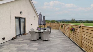 A patio with a table and chairs, a wooden fence, and a view of the countryside. - Clarmes House (Limavady)