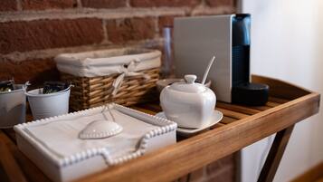 A wooden table with a white tray, a white sugar bowl, and a white sugar container. There are also two white mugs and a wicker basket in the background.