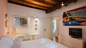 Une chambre à coucher comprenant un lit, un bureau, un téléviseur et un tableau abstrait aux couleurs vives.