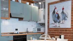 Une cuisine moderne avec une table de salle à manger ronde, des chaises transparentes et un tableau représentant des poulets accroché au mur.