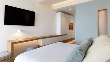 Una habitación de hotel moderna con una cama grande, una mesita de noche con lámpara, un televisor de pantalla plana en la pared y un cabecero de madera.