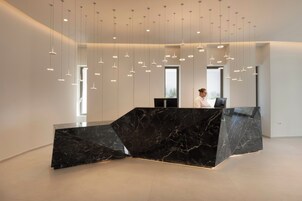 Un mostrador de recepción moderno con acabado de mármol negro, varias lámparas colgantes y un amplio ventanal que proporciona luz natural.