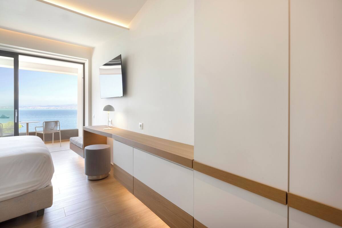 Ein modernes Hotelzimmer mit einem großen Bett, einem Schreibtisch, einem Stuhl und Meerblick.