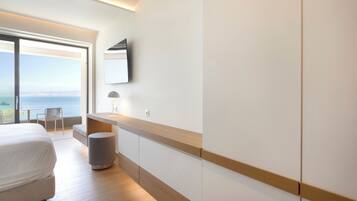 A modern hotel room with a large bed, a desk, a chair, and a view of the sea.