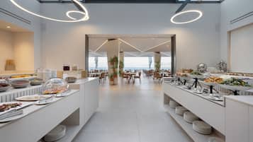 A modern dining area with a central open space, surrounded by tables and chairs, with a view of the sea through large windows.
