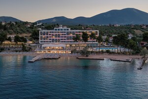 Un hotel con piscina, varios pisos y vistas a montañas al fondo.