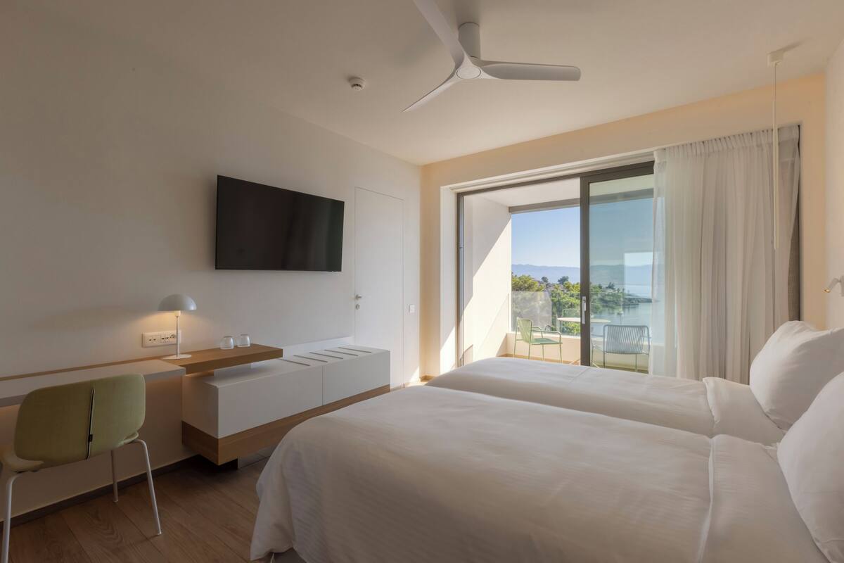 Ein modernes Hotelzimmer mit Bett, Schreibtisch, Stuhl, Fernseher und einem Balkon mit Blick.