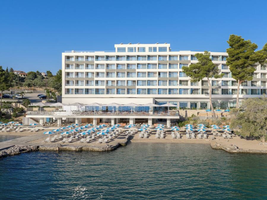 Et moderne hotel med flere etager, et poolområde med liggestole og udsigt til havet.