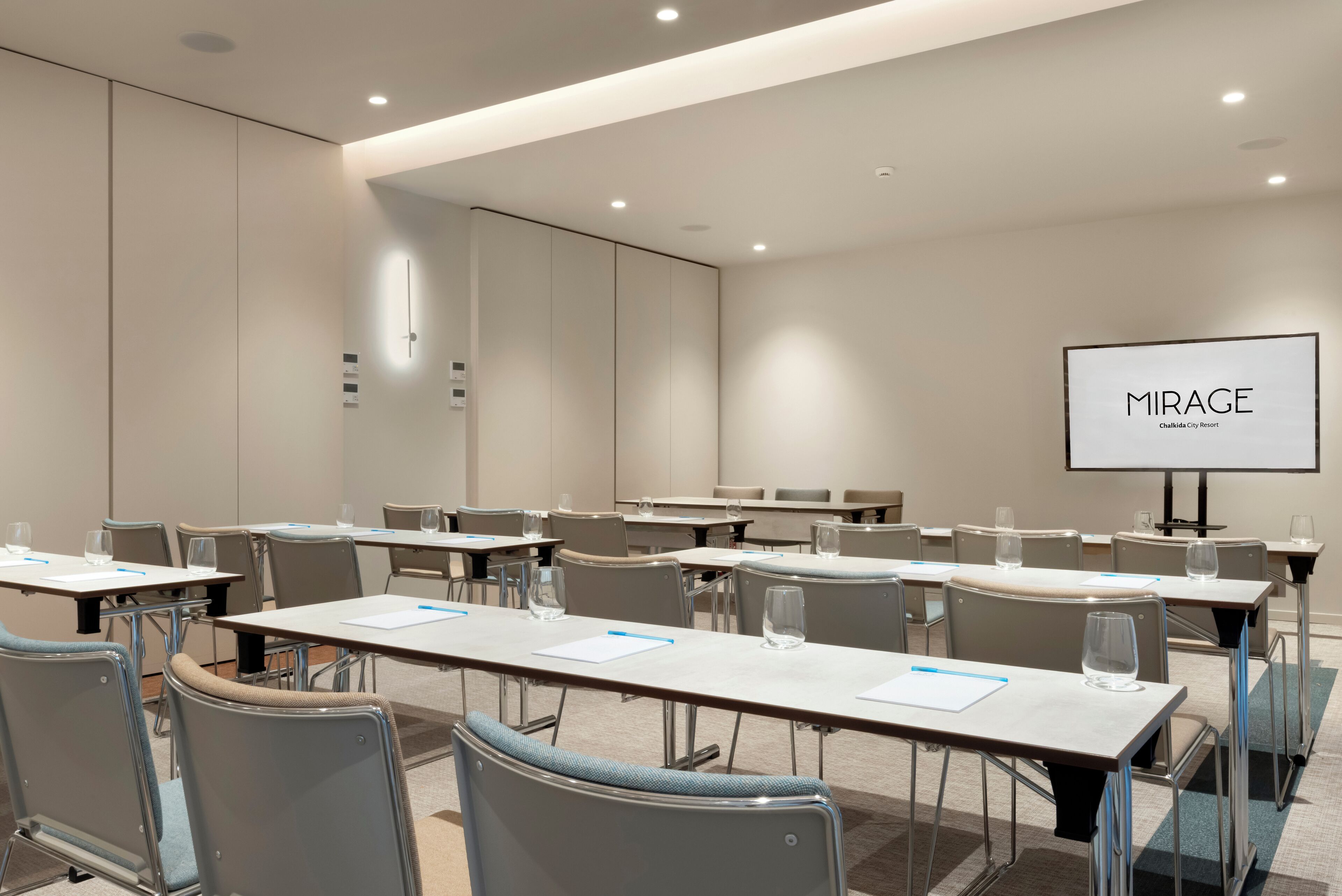 A conference room with tables, chairs, a projector screen, and a sign reading "MIRAGE."