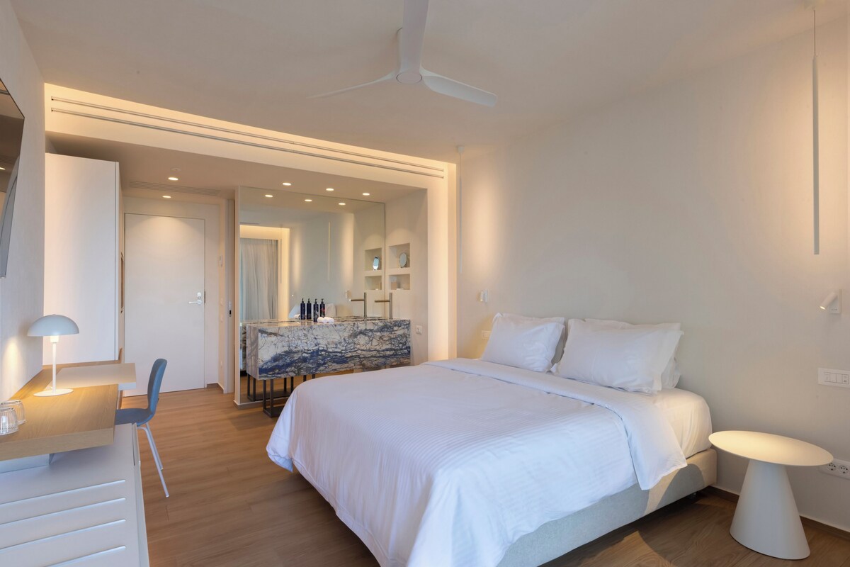 Een moderne slaapkamer met een groot bed, nachtkastjes, een bureau met stoel en een plafondventilator.