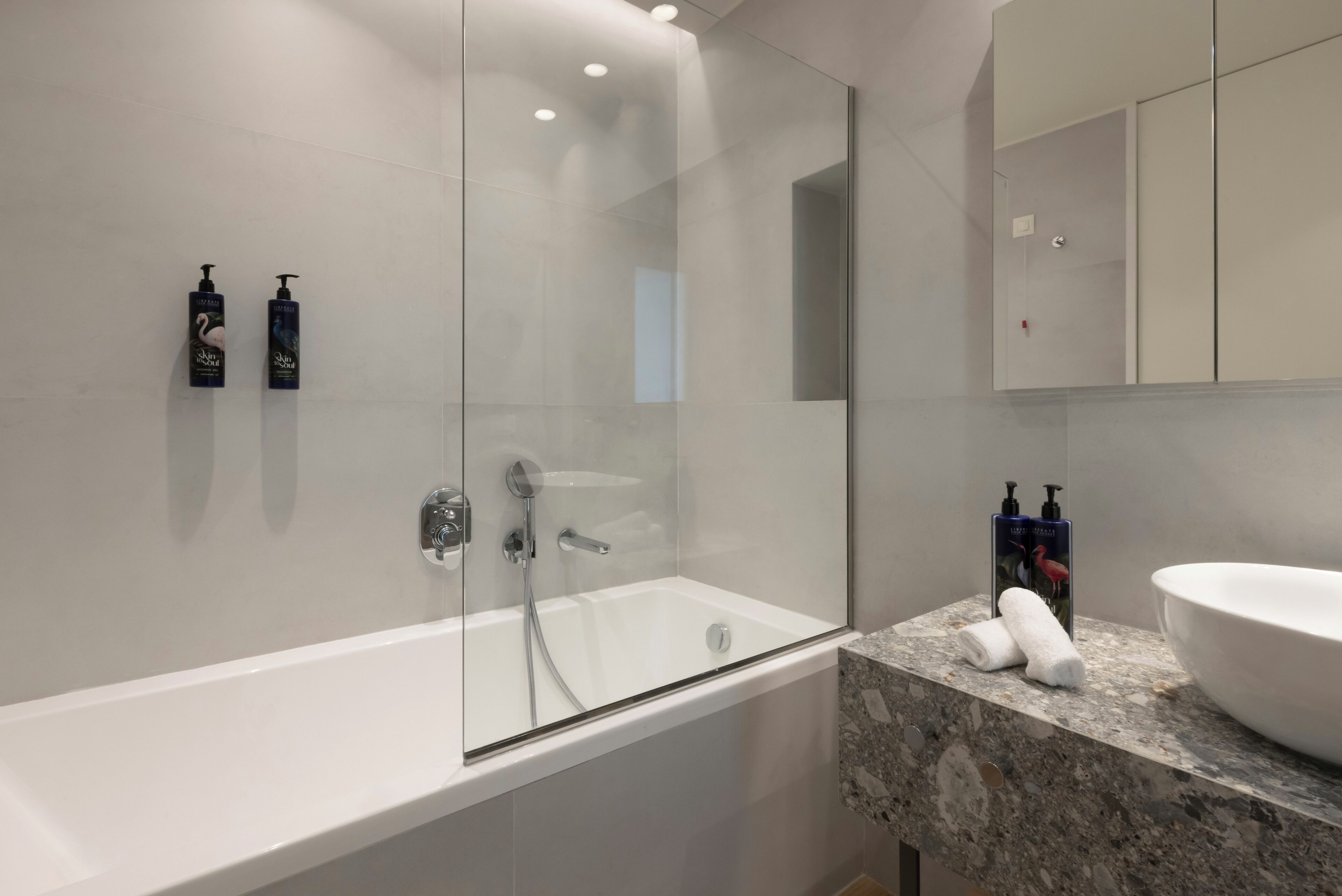 A modern bathroom with a glass-enclosed shower, a white bathtub, and a marble countertop.