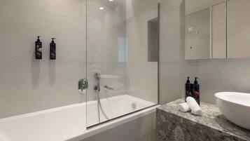 A modern bathroom with a glass-enclosed shower, a white bathtub, and a marble countertop.