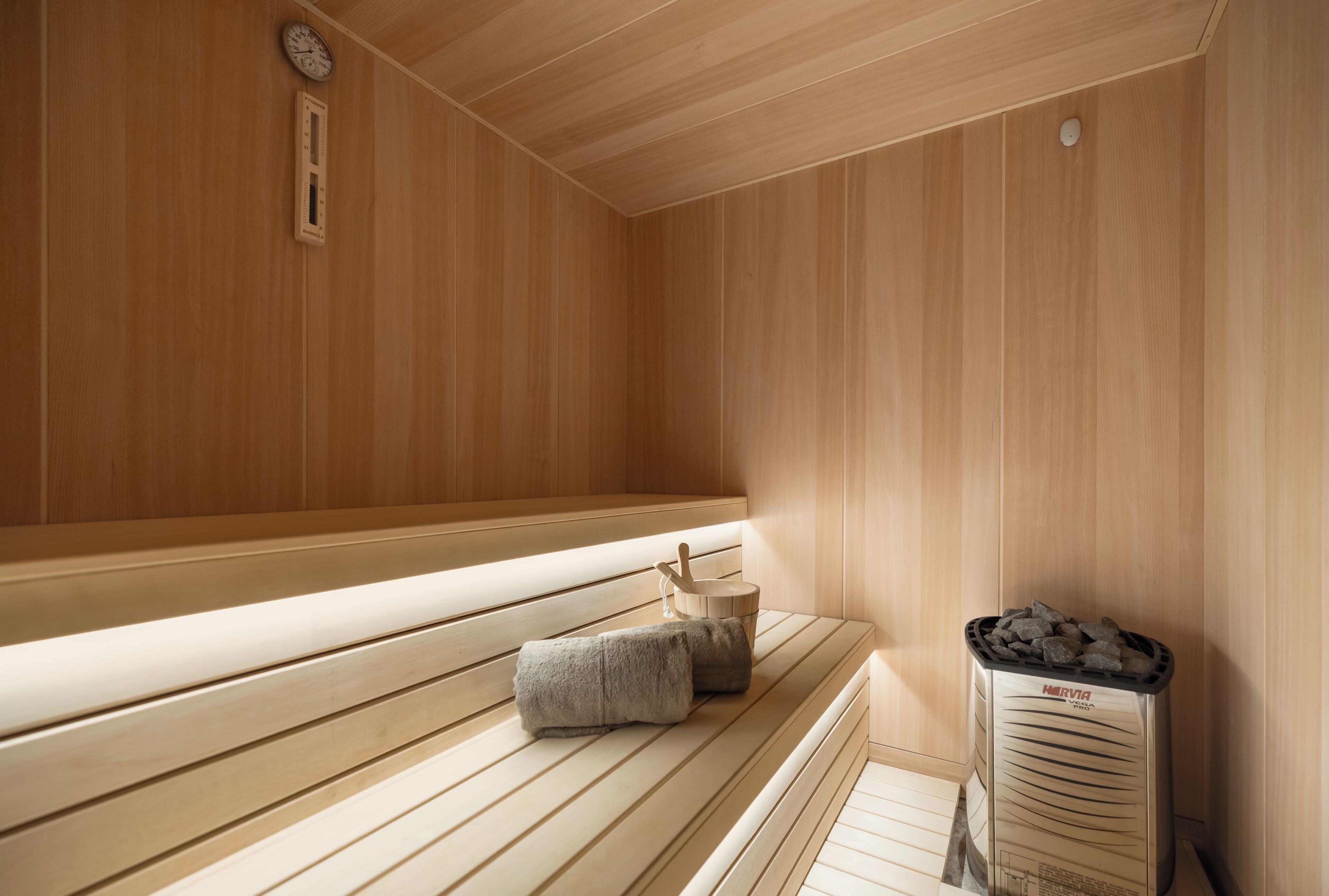 A sauna room with wooden benches, a towel, and a sauna heater.