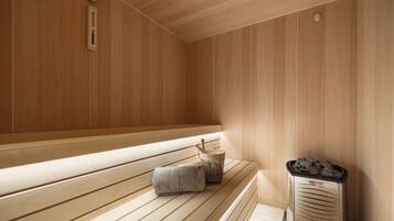 A sauna room with wooden benches, a towel, and a sauna heater.