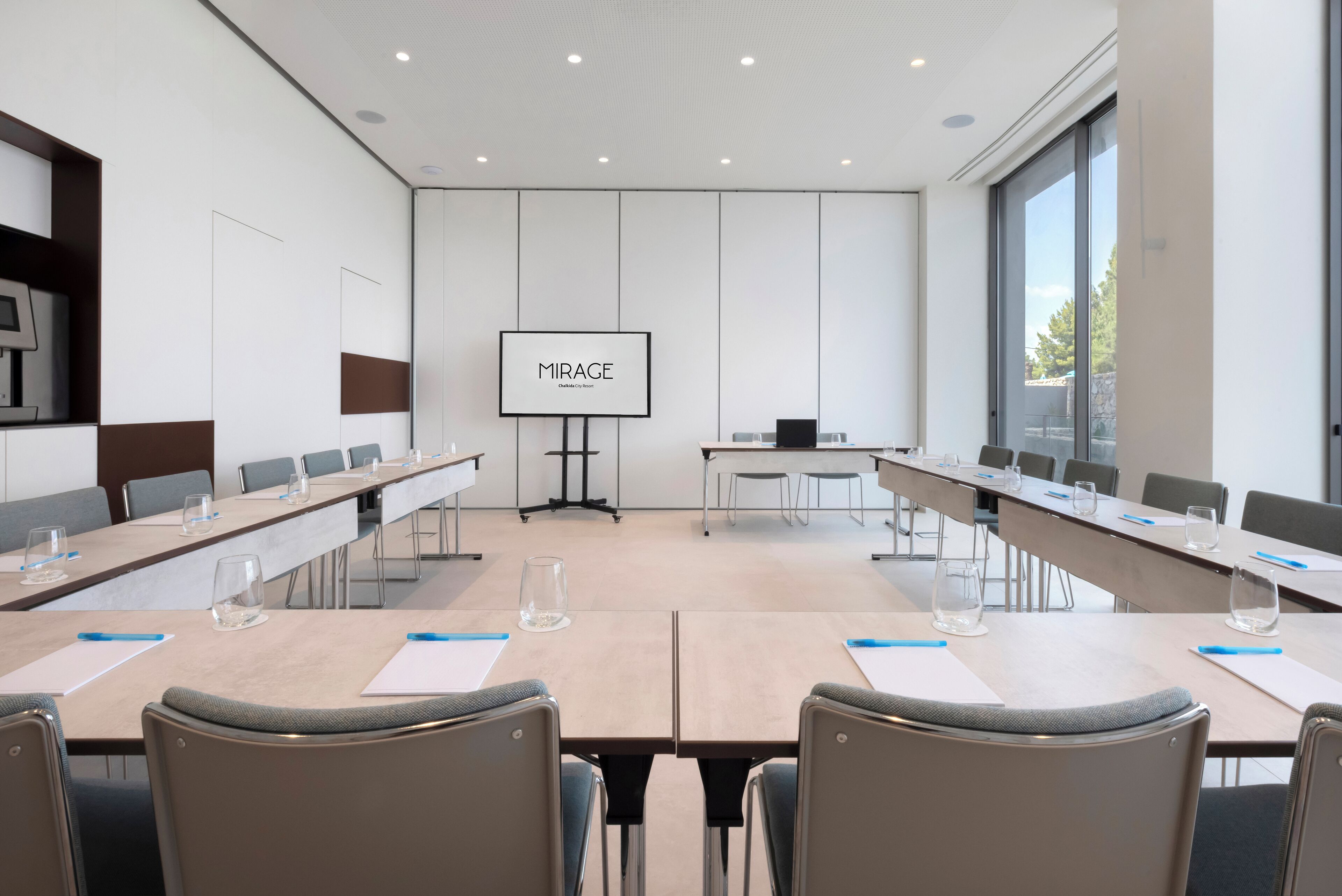 Una sala de conferencias con una larga mesa, sillas, una pantalla y un proyector.