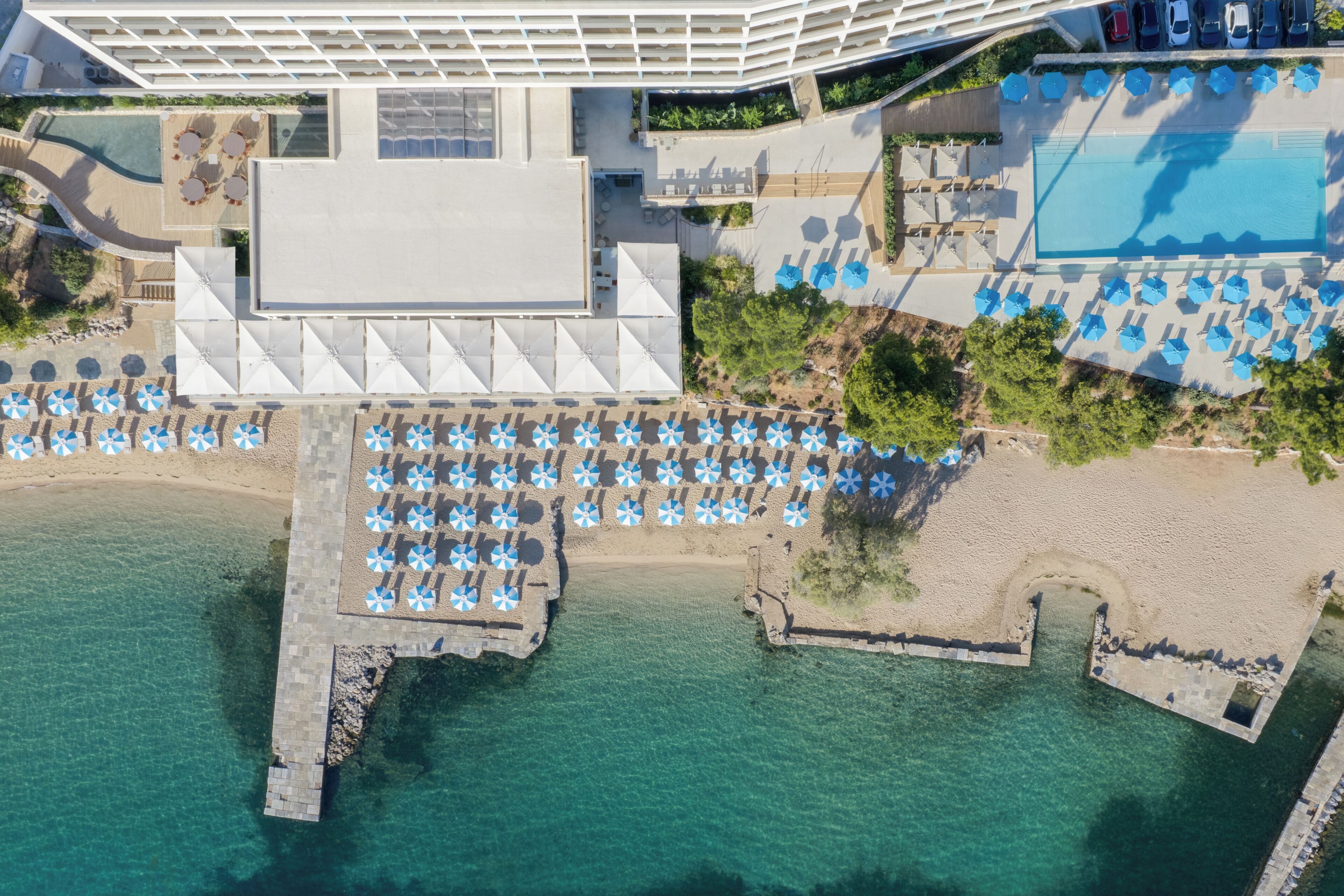 An aerial view of a resort with a pool, beach umbrellas, and a pier.