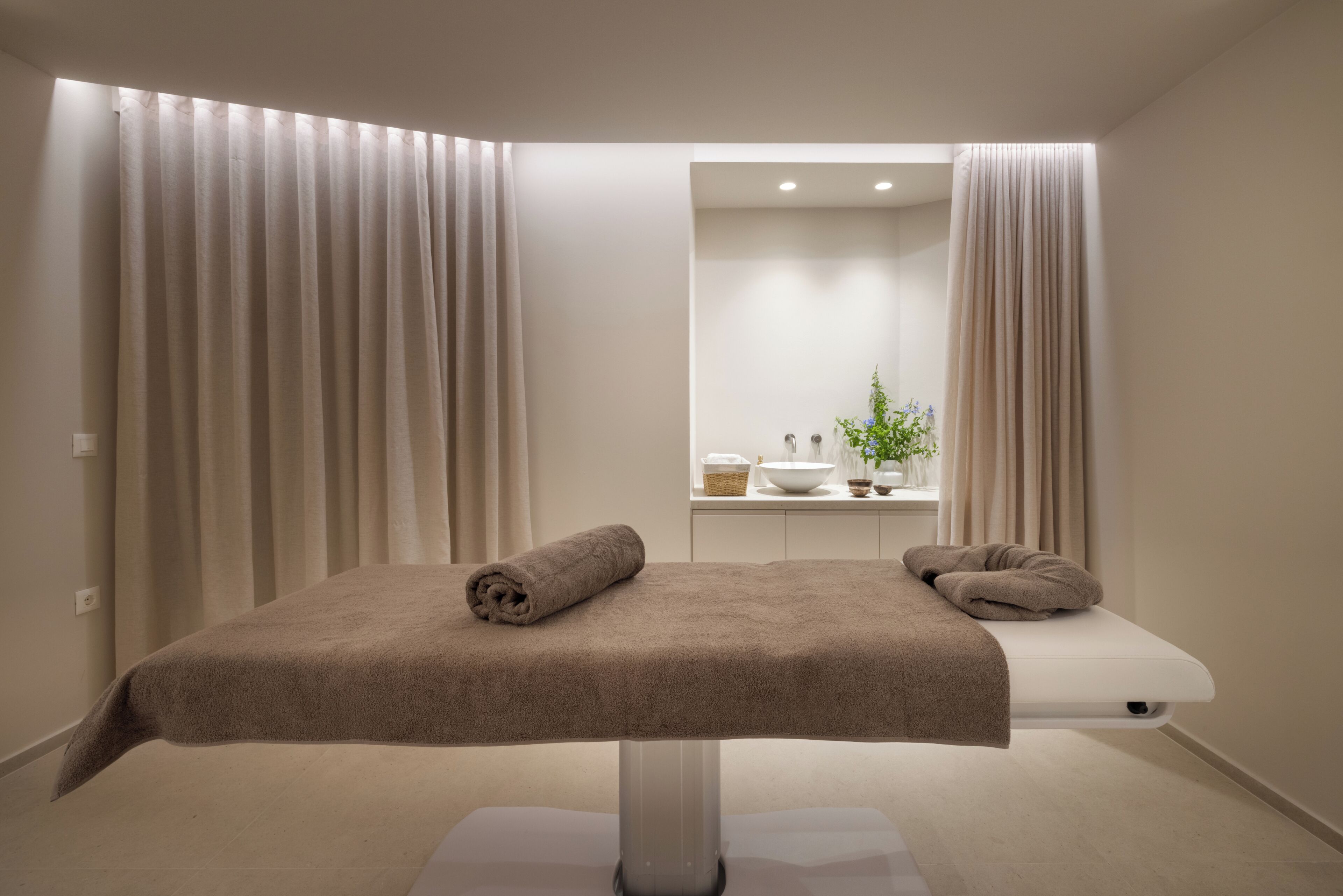 A spa room with a massage table, two towels, a sink, and a plant.