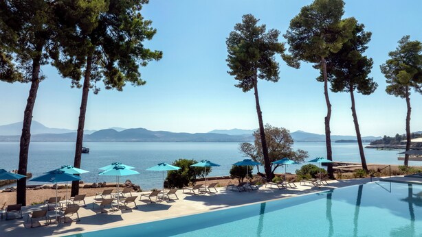 Un espace aménagé au bord de la piscine, avec des chaises longues et des parasols, offrant une vue sur une étendue d’eau et, au loin, sur des montagnes.
