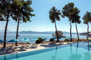 A poolside area with lounge chairs and umbrellas, overlooking a body of water with mountains in the distance. - Mirage Chalkida City Resort (Chalcis)