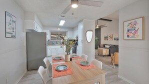 A modern kitchen with white cabinets, a grey refrigerator, and a dining area with a wooden table set for four.