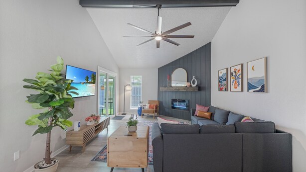 A modern living room with a gray sofa, a wooden coffee table, a potted plant, and a flat-screen TV.
