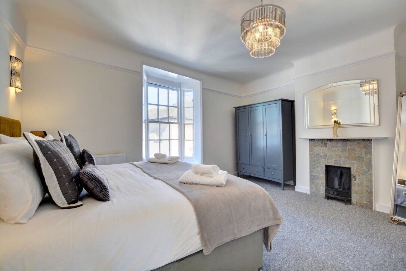 A bedroom with a large bed, a wardrobe, a fireplace, and a chandelier.