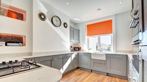 A modern kitchen with a gas stove, grey cabinets, a microwave, and a window with an orange blind.