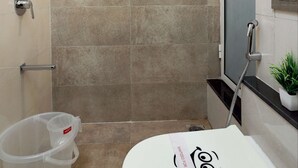 A bathroom with beige tiles, a shower, a toilet, a trash bin, and a small plant. - 3 BHK Suite (Gagal Home) (Mumbai)