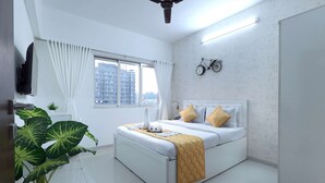 A modern bedroom with a bed, a ceiling fan, a window with curtains, a wall clock, and a potted plant. - 3 BHK Suite (Gagal Home) (Mumbai)