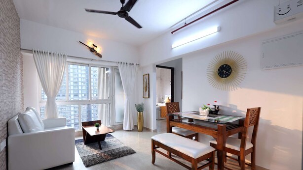 A modern living room with a sofa, a dining table with chairs, a ceiling fan, and a large window with curtains. - 3 BHK Suite (Gagal Home) (Mumbai)