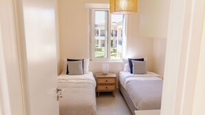 Un dormitorio con dos camas, una ventana y una mesita de noche con lámpara.