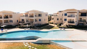Un resort con una gran piscina, edificios de varios pisos, balcones y sillones de descanso.