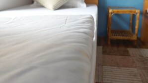 A bed with a wooden headboard, a white pillow, and a small wicker chair beside it. - Cozy place in Patan (Lalitpur)