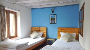 A room with two wooden beds, a small table, and a window with curtains. - Cozy place in Patan (Lalitpur)