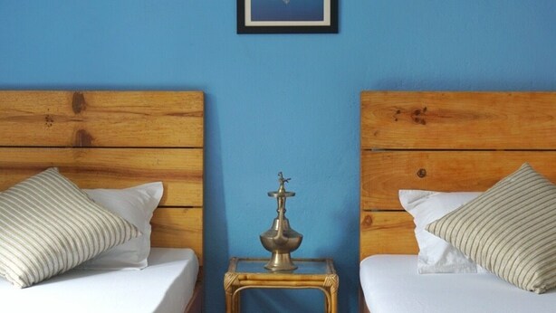 A room with two wooden beds, a small table with a lamp, and a framed picture on the wall. - Cozy place in Patan (Lalitpur)