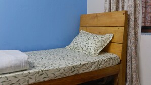 A single bed with a patterned mattress, a wooden headboard, and a pair of slippers on the floor. - Cozy place in Patan (Lalitpur)