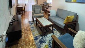 Ein Wohnzimmer mit Sofa, Sessel, Couchtisch, Fernseher und Deckenventilator.
