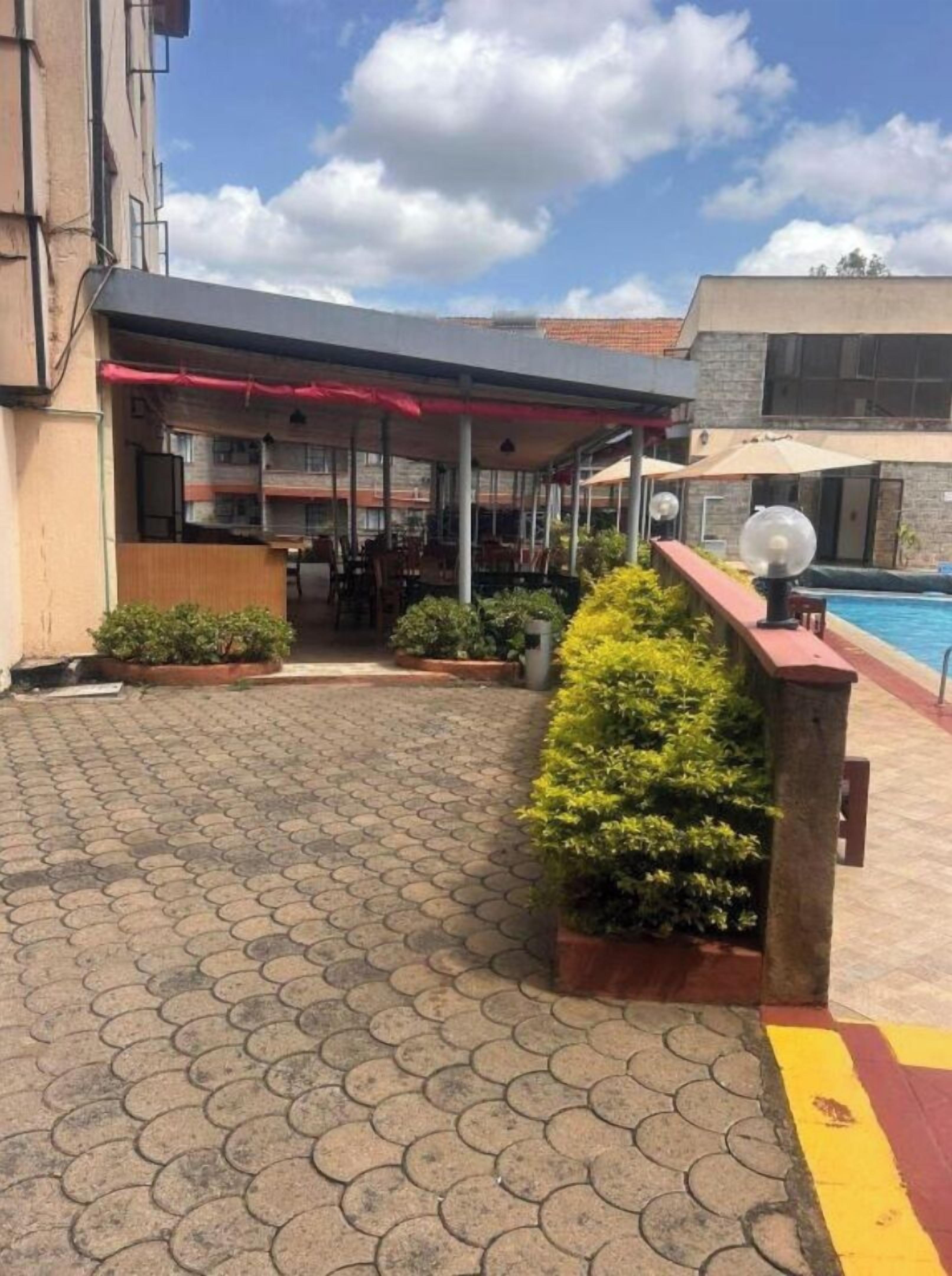 An outdoor patio area with a pool, covered seating, and potted plants.