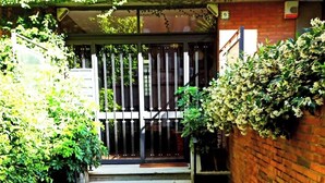 Un camí estret que condueix a un accés tancat per una reixa metàl·lica i un petit porxo.